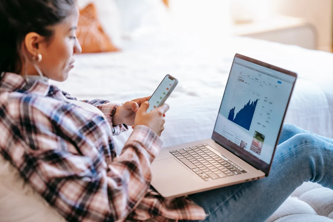 A woman using her phone and laptop for crypto investment